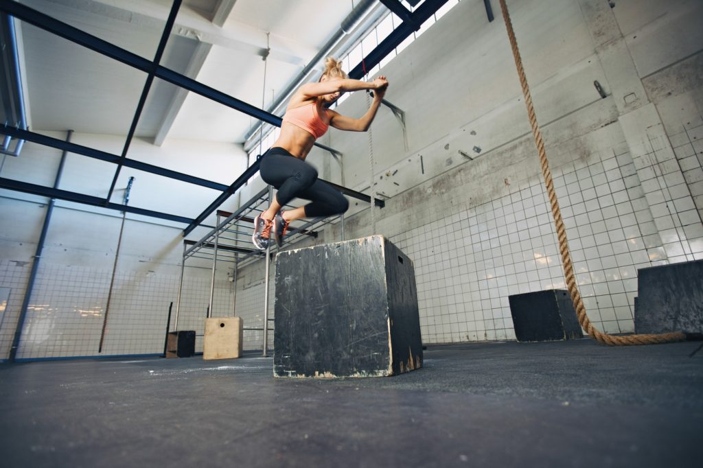 Fit woman is performing box jumps at gym